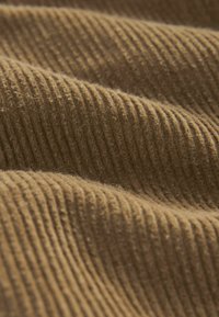 Gros plan sur un tissu en velours côtelé marron doux montrant des ridules parallèles et une surface texturée avec des plis légers.