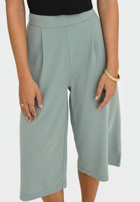 Jasnozielone kuloty wykonane z gładkiego materiału, z wysokim stanem, z plisami z przodu oraz szerokimi, ściętymi nogawkami.