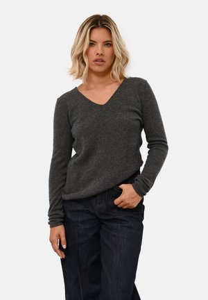 Grijze v-hals trui van zachte breigoed. Lange mouwen met strakke manchetten, gedragen met donkere denim jeans. Eenvoudig en minimalistisch ontwerp.