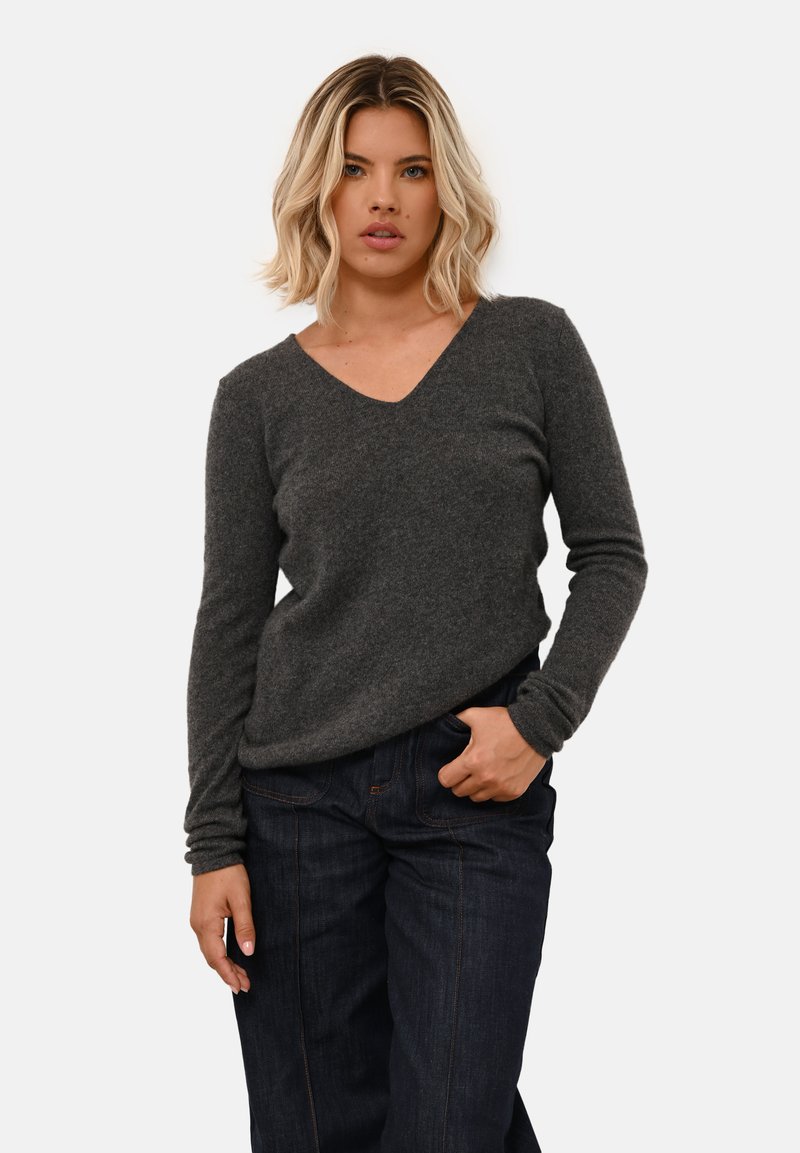 Grijze v-hals trui van zachte breigoed. Lange mouwen met strakke manchetten, gedragen met donkere denim jeans. Eenvoudig en minimalistisch ontwerp.