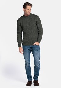 Donkergroen gebreide trui met een ronde hals, gecombineerd met blauwe jeans en bruine suède enkellaarsjes. De trui heeft een geribbelde textuur.