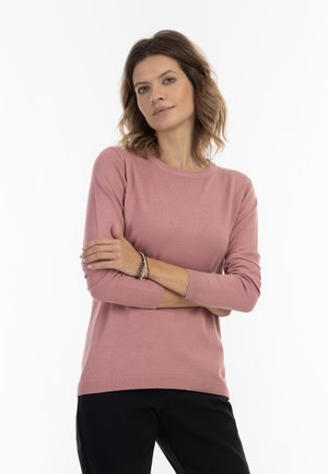 Jasnoróżowy sweter dzianinowy z okrągłym dekoltem i rękawami o długości trzech czwartych, z prążkowanym wykończeniem. Połączony z czarnymi spodniami.