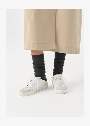 Valged ja hallid tennised musta kannaaktsendiga, millel on sile nahkpealis ja tekstuuriga sametine varvas. Kanda tumedate hallide viltuste sokkidega.