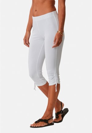 White capri leggings made of soft, stretchy fabric with a cinched hem detail. Paired with black flat sandals.