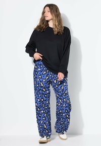 Sweatshirt noir surdimensionné associé à un pantalon bleu à imprimé léopard ample. La tenue présente une texture lisse et un design décontracté.