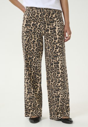 Pantalon large à imprimé léopard beige et noir, porté avec des ballerines noires et un haut blanc.