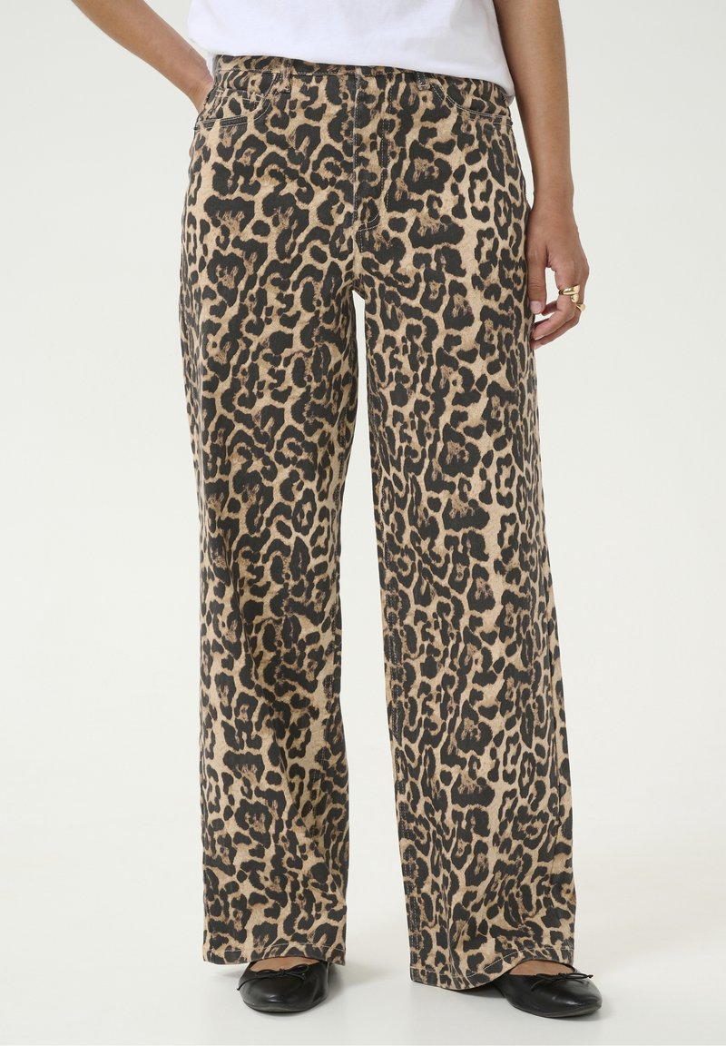 Pantalon large à imprimé léopard beige et noir, porté avec des ballerines noires et un haut blanc.
