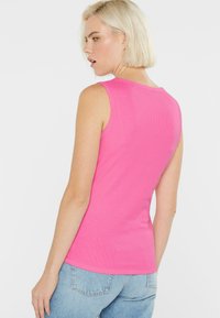 Enganliegendes, ärmelloses rosa Tanktop aus geripptem Stoff, mit rundem Halsausschnitt und glatter Textur, kombiniert mit hellblauen Jeans.