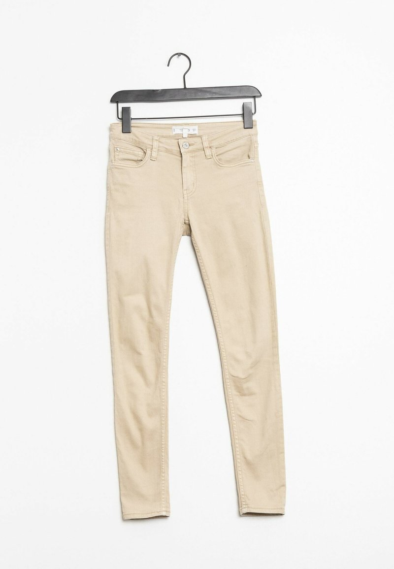 Jean skinny beige en mélange de coton, avec une taille haute, cinq poches et une fermeture à bouton à l'avant. Suspendu à un crochet en plastique noir.