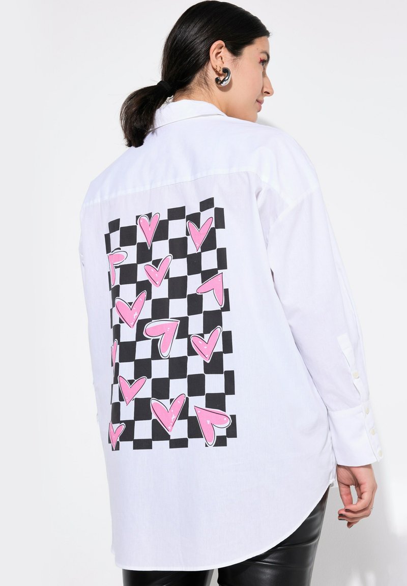 Maglietta bianca a maniche lunghe con una grafica a scacchi bianca e nera e cuori rosa sul retro. Dettagli con bottoni sulle maniche.