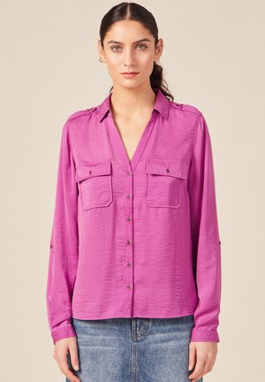 Camicia button-down a maniche lunghe di un brillante colore rosa, con due tasche frontali, scollatura a V e polsini arrotolati con dettagli di bottoni.