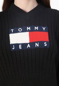 Czarny sweter z prążkowaną strukturą, z wyraźnym logo Tommy Jeans, w niebieskim, czerwonym i białym kolorze w prostokątnym wzorze z przodu.