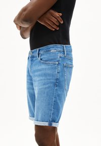 Shorts en denim bleu clair avec des revers, design à cinq poches et fermeture à bouton en métal. Texture lisse et coupe classique.