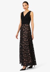 Schwarzes Kleid mit V-Ausschnitt und ärmellosem Design, mit einem durchsichtigen Rock, der mit einem geometrischen schwarzen Muster verziert ist. In voller Länge gemessen.