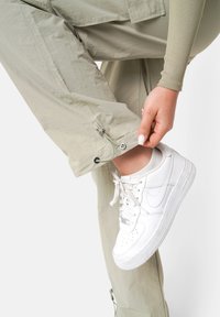 Lichtbeige cargobroek met elastische boorden en aanpassers, gecombineerd met witte Nike sneakers. Focus op pasvorm en materiaale Textuur.