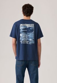 Μπλουζάκι από βαμβάκι σε ναυτικό μπλε χρώμα με γραφικό σχέδιο στην πλάτη που παρουσιάζει τοπία, κείμενο και το λογότυπο της Levi's. Κοντά μανίκια και άνετη εφαρμογή.