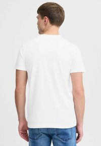 Hvid t-shirt med korte ærmer og rund hals, vist fra bagsiden, lavet af blødt bomuldsstof, parret med blå denim jeans.