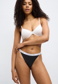 Λευκό επενδεδυμένο σουτιέν με λεπτές τιράντες, σετ με μαύρο στρινγκ με λευκή λωρίδα με το λογότυπο "TOMMY HILFIGER". Λείο υφασμάτινο υλικό.