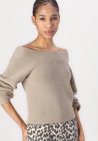 Beige off-the-shoulder knitted sweater with ribbed texture and long, slightly puffed sleeves. Paired with leopard print jeans.