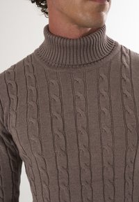 Brązowy sweter z kołnierzem typu golf z dzianiny w warkocze, o prążkowanym kołnierzu, textured wzorze i dopasowanym kroju, podkreślający rzemiosło i ciepło.