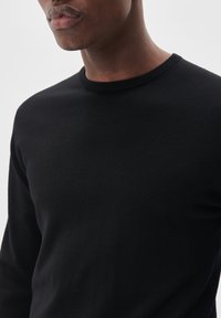 Melnas adītas džemperis ar apaļu kaklu, kuram ir gluda tekstūra un pieguļošs dizains, koncentrējoties uz ķermeņa un kakla detaļām.