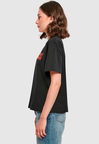 Schwarzes Baumwoll-T-Shirt mit kurzen Ärmeln, versehen mit einem roten Grafikdesign auf der Vorderseite. Es hat einen lockeren Schnitt und einen runden Halsausschnitt.