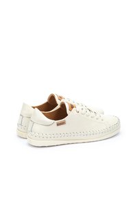 Zapatillas de piel blanca con un detalle trenzado texturizado alrededor de la suela, contrastadas por un acento de piel marrón en la lengüeta. Hardware plateado visible.