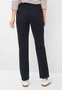 Jean noir taille haute avec une coupe droite. Deux poches plaquées à l'arrière. Porté avec des chaussures blanches aux accents métalliques.