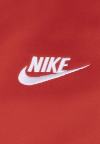 Tessuto rosso con una finitura testurizzata che presenta un logo Nike ricamato in bianco e un design a swoosh sotto il nome del marchio.
