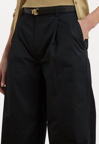Black pleated trousers with a smooth texture, paired with a black textured belt featuring a gold logo buckle.