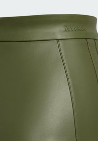 Olivgründer Kunstlederrock mit glatter Textur, der ein erhaben aufgetragenes "IVY PARK"-Logo und sichtbare Nähte aufweist.