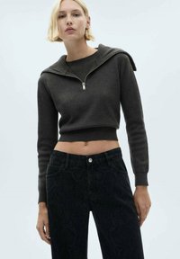 Mörkgrå zip-up kort hoodie, kombinerad med hög midja svarta jeans med en subtilt mönster. Slät textur.