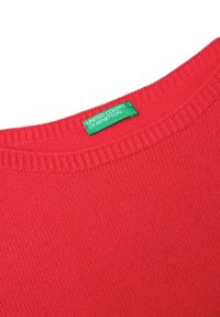 Tela de punto roja con cuello de canalé y una etiqueta de ropa verde que dice "United Colors of Benetton" cosida en el interior del escote.