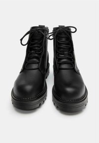 Bottines en cuir noir avec bout arrondi, surface texturée et laçage à l'avant. Semelle épaisse en caoutchouc avec un détail de surpiqûres accentuées.