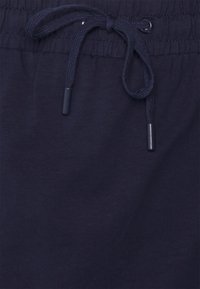 Calções de algodão azul-marinho com um cós elástico ajustável com cordão de tecido correspondente e pontas de metal, textura suave e sem padrões visíveis.