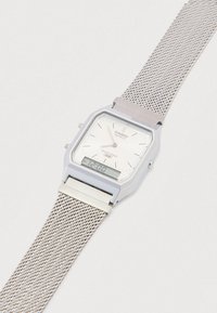 Srebrny zegarek Casio z kwadratową tarczą, białą tarczą z oznaczeniami godzin i siateczkową bransoletą. Cyfrowy wyświetlacz na dole. Wodoodporny.