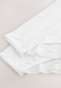 Deux paires de sous-vêtements blancs pour femmes avec bordure en dentelle pliées sur un fond neutre.