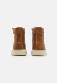 Hnědé kožené kotníkové boty s texturovaným povrchem, s béžovou gumovou podrážkou, zadním poutkem a jemnými detaily šití.