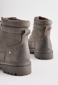 Botas de tobillo de cuero gris con un collar enrollado, costuras en contraste y suelas de goma texturizadas con profundas estrías para mejorar la tracción.