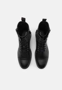Botines de cuero negro con cordones, paneles laterales elásticos y cierre de cremallera. Presentan una puntera redondeada y detalles de costura en contraste.