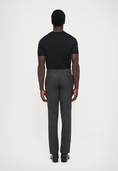 Camisa negra de manga corta combinada con pantalones gris ajustados. Los pantalones presentan un sutil patrón y bolsillos traseros. Se lleva con zapatos negros.
