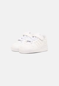 White sneakers with a smooth leather upper, textured toe cap, and velcro strap. Features perforated accents and a rubber sole with grip.