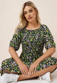 Kukkamallinen midi-mekko, jossa musta tausta ja purppuran ja keltaisen värisiä kukkia, rypytetty yläosa ja puffihihat, yhdistettynä valkoisiin lenkkareihin.