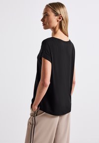 Sort kortærmet bluse med rund halsudskæring, blødt stof og en afslappet pasform, parret med beige bukser med sorte sidestriber.
