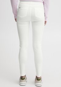 Bele skinny jeans z gladko teksturo, pet žepov in visokim pasom. Nosi jih skupaj z udobnimi supergami z zelenimi detajli.