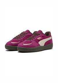 Sneakers viola in suede con lacci e dettagli marroni. Presentano una striscia laterale bianca e una suola in gomma testurizzata. Logo del marchio sul lato.