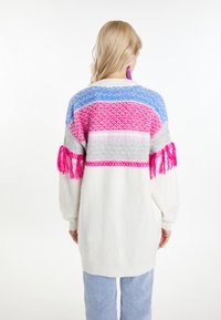 Överdimensionerad vit tröja med flerfärgade stickade mönster i rosa, blått och grått. Har texturerade fransdetaljer på ärmarna.