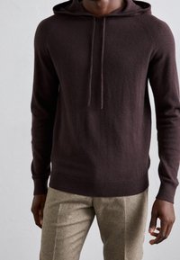 Brun hoodie i mjukt tyg med en ficka fram, snörning i huvan, ribbade muddarna och rak fåll, ihop med ljusbruna byxor.