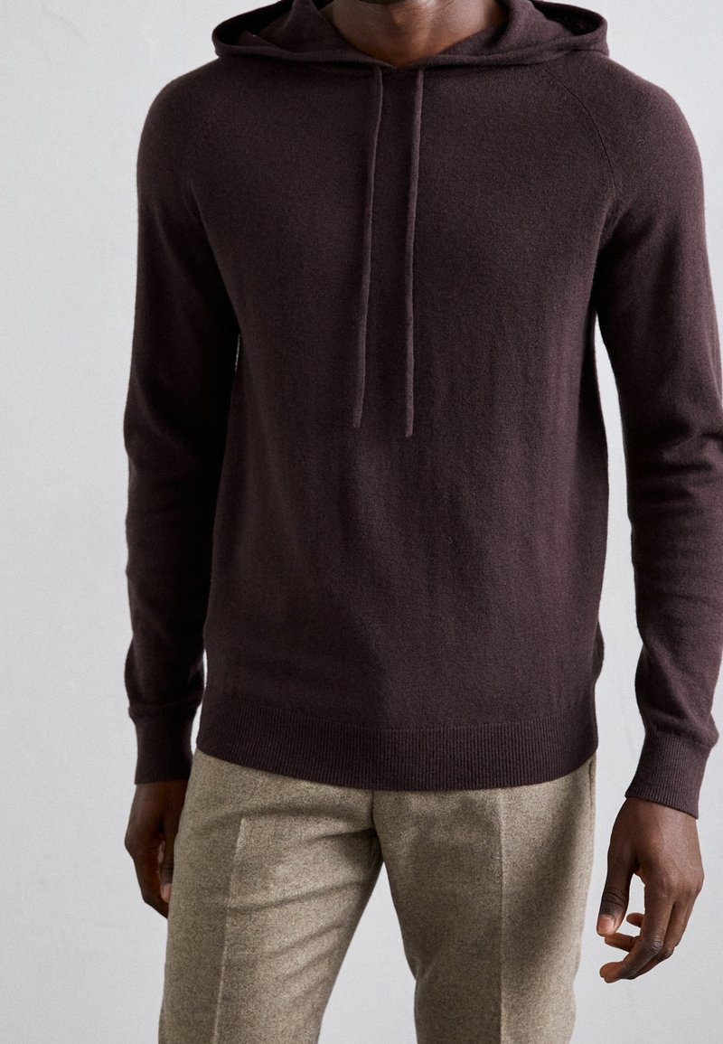 Brun hoodie i mjukt tyg med en ficka fram, snörning i huvan, ribbade muddarna och rak fåll, ihop med ljusbruna byxor.