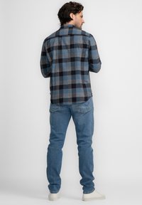 Camisa de franela a cuadros azules y grises con cuello clásico y puños abotonados, combinada con pantalones vaqueros de denim azul claro y zapatillas blancas.